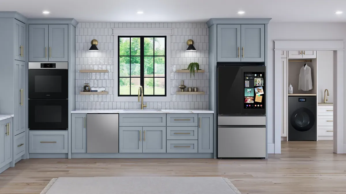 A wide shot of a kitchen with light blue cabinets and a smart oven, dishwasher and refrigerator. 